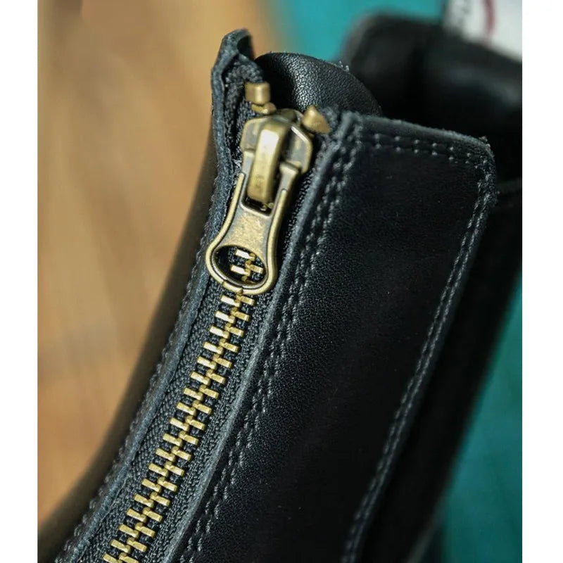 Black leather boot with a zipper on a gray surface . Ghoddosh
