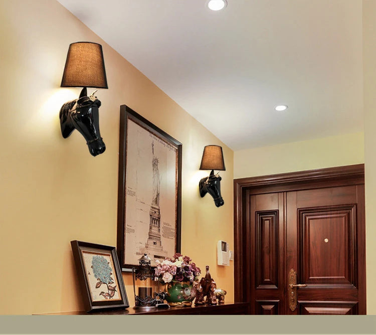 Decorative wall sconces with horse heads on a wall with framed pictures and a wooden door. ghoddosh.com