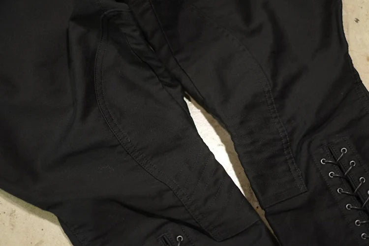 Close-up of black pants or a skirt with a lace-up side detail, laid flat on a light surface. @ ghoddosh.com