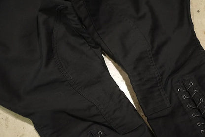 Close-up of black pants or a skirt with a lace-up side detail, laid flat on a light surface. @ ghoddosh.com